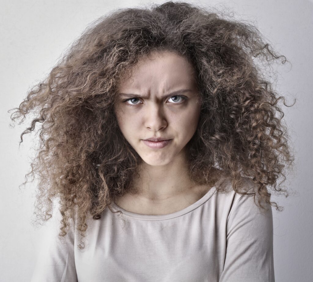 Portrait of a woman with curly hair showing an angry facial expression. Ideal for emotion-based content.